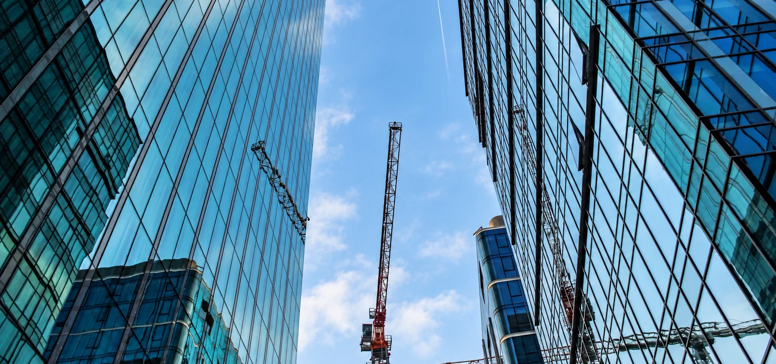 Construction cranes between glass-fronted commercial buildings